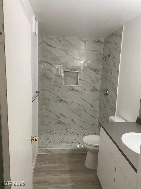 bathroom with toilet, vanity, wood-type flooring, and tiled shower