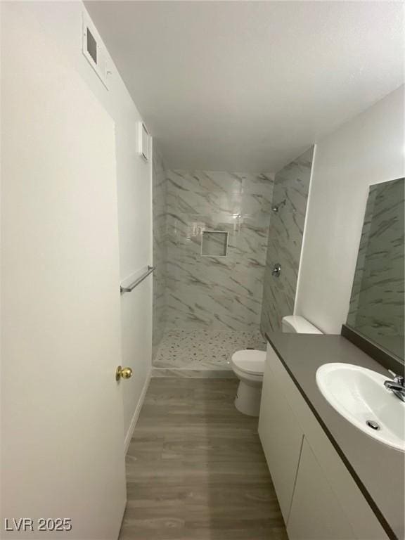 bathroom featuring toilet, vanity, hardwood / wood-style floors, and tiled shower