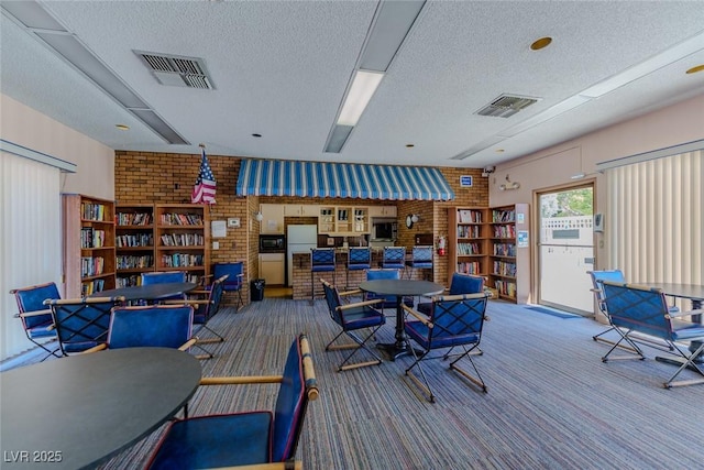 dining room featuring carpet flooring, a textured ceiling, and brick wall