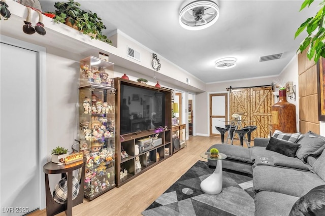 living room with ornamental molding, a barn door, wood finished floors, and visible vents