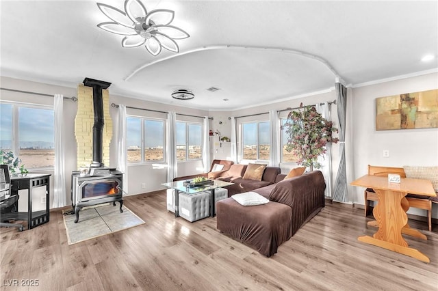 living room featuring visible vents, ornamental molding, wood finished floors, and a wood stove