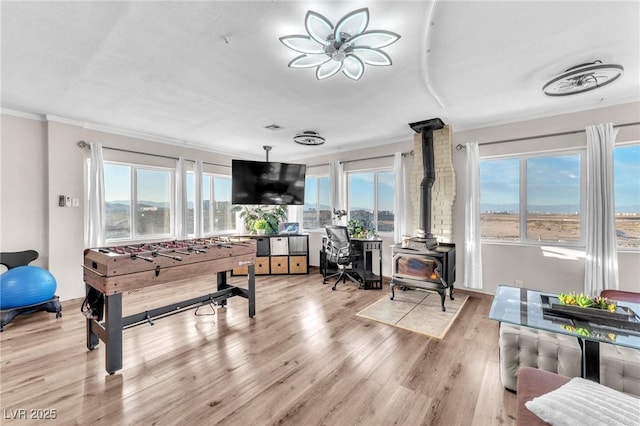 rec room featuring a wood stove, ornamental molding, and light wood-style flooring