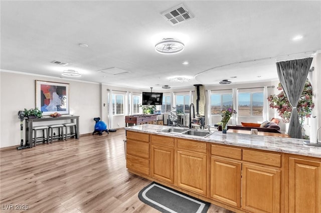 kitchen with light wood finished floors, visible vents, light stone counters, crown molding, and a sink