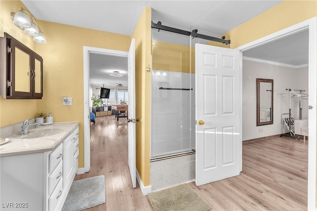 bathroom with ornamental molding, a shower with shower door, vanity, wood finished floors, and baseboards