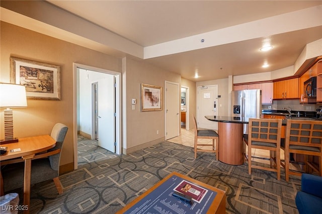 interior space featuring dark colored carpet, stainless steel fridge, kitchen peninsula, and a breakfast bar area