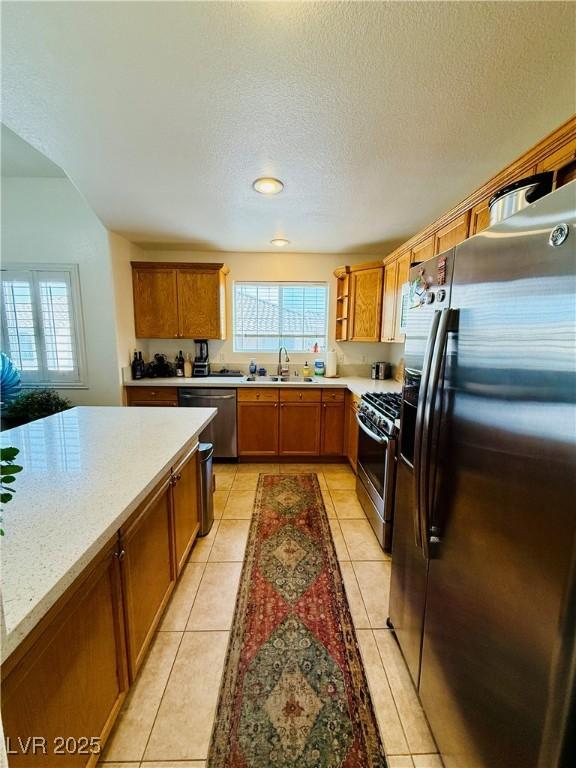 kitchen featuring light stone countertops, sink, a textured ceiling, light tile patterned floors, and appliances with stainless steel finishes