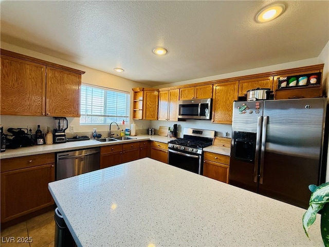 kitchen with sink, stainless steel appliances, light stone counters, dark tile patterned floors, and a textured ceiling