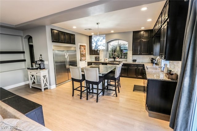 kitchen with pendant lighting, a center island, light hardwood / wood-style flooring, light stone countertops, and stainless steel built in refrigerator