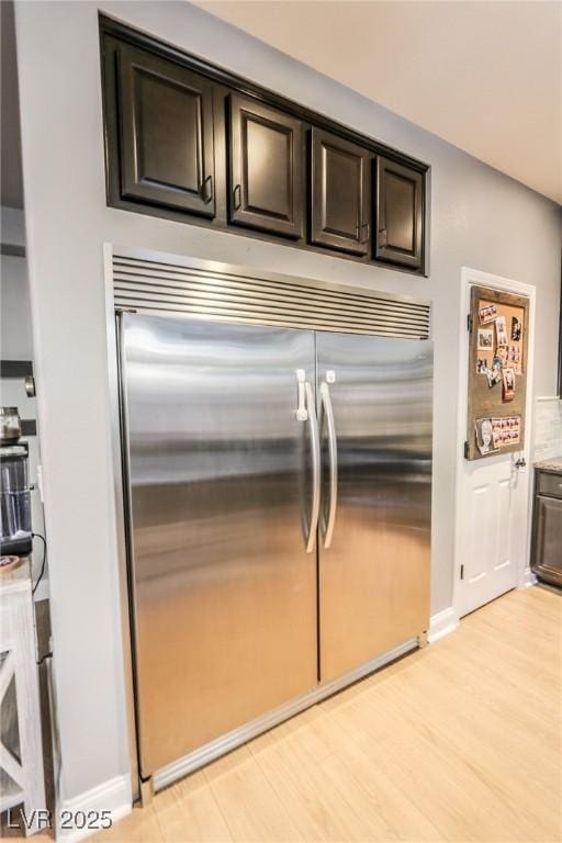 kitchen featuring tasteful backsplash, dark brown cabinets, stainless steel built in refrigerator, and light hardwood / wood-style flooring