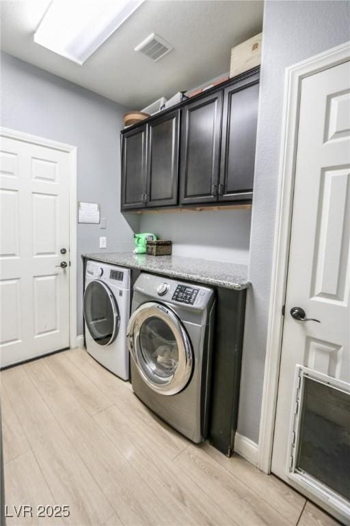 laundry room featuring cabinets, light wood-type flooring, and washing machine and dryer