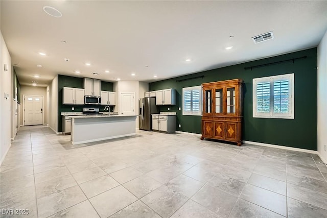 kitchen with a center island with sink, sink, light tile patterned floors, stainless steel appliances, and white cabinets