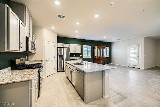 kitchen featuring sink, an island with sink, gray cabinetry, stainless steel appliances, and light stone counters