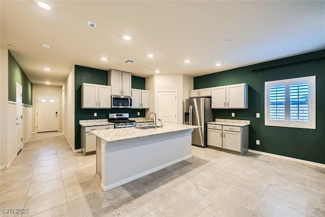 kitchen with sink, appliances with stainless steel finishes, an island with sink, white cabinets, and light stone counters