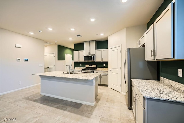 kitchen with light tile patterned floors, a center island with sink, stainless steel appliances, light stone countertops, and sink