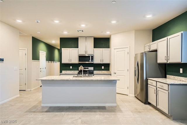 kitchen featuring appliances with stainless steel finishes, sink, light stone counters, and a center island with sink