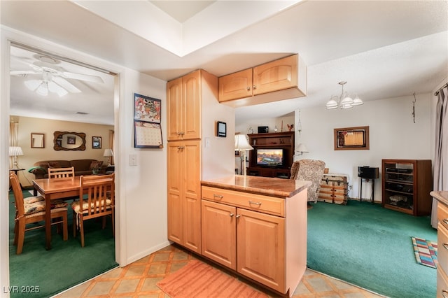 kitchen featuring light carpet, light brown cabinets, ceiling fan with notable chandelier, and pendant lighting