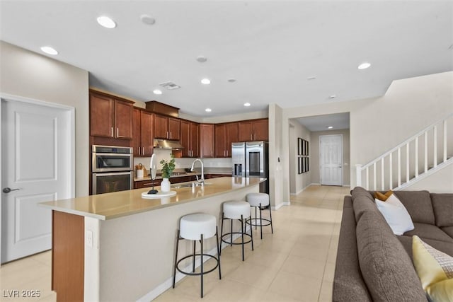 kitchen featuring sink, a kitchen breakfast bar, light tile patterned floors, an island with sink, and appliances with stainless steel finishes