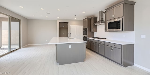 kitchen with a wealth of natural light, a kitchen island with sink, wall chimney exhaust hood, and appliances with stainless steel finishes