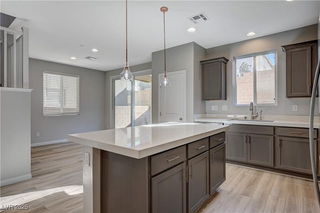 kitchen with sink, hanging light fixtures, light hardwood / wood-style flooring, a kitchen island, and a healthy amount of sunlight