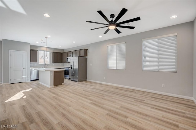 kitchen with ceiling fan, appliances with stainless steel finishes, hanging light fixtures, a center island, and light wood-type flooring