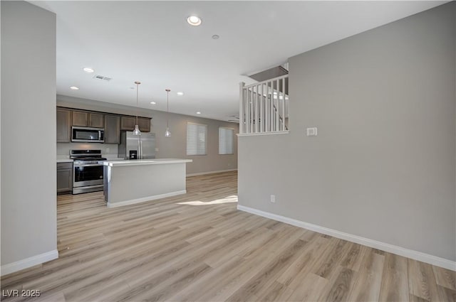 kitchen featuring dark brown cabinets, hanging light fixtures, light wood-type flooring, appliances with stainless steel finishes, and a kitchen island