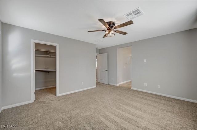 unfurnished bedroom featuring ceiling fan, a spacious closet, a closet, and light carpet