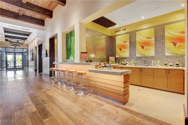 bar with sink, beam ceiling, decorative backsplash, wooden ceiling, and light wood-type flooring