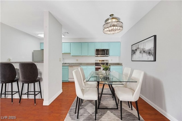 dining room with sink, wood-type flooring, and a notable chandelier