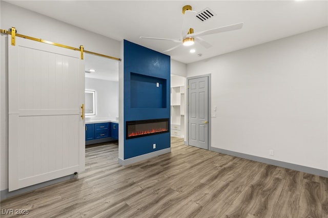 unfurnished bedroom featuring a large fireplace, ceiling fan, a barn door, hardwood / wood-style floors, and connected bathroom