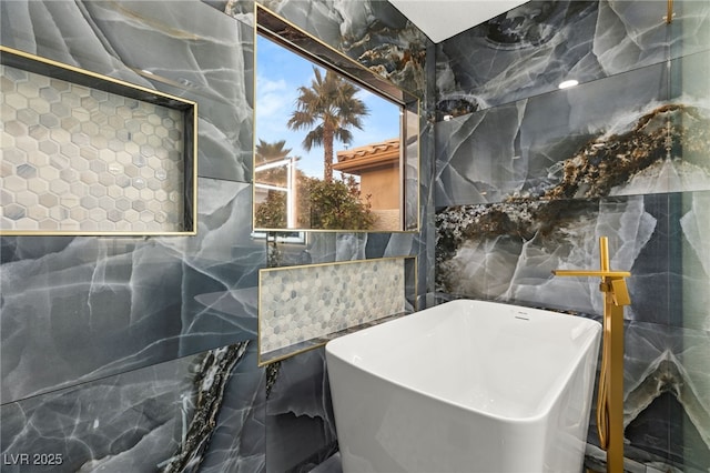 bathroom featuring a bath, plenty of natural light, and tile walls