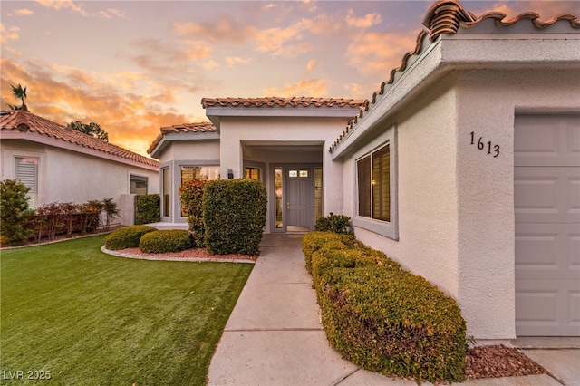 exterior entry at dusk featuring a yard and a garage