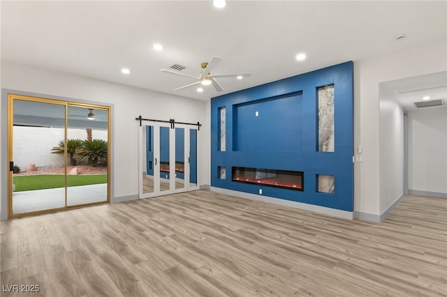 unfurnished living room with a fireplace, a barn door, light hardwood / wood-style floors, and ceiling fan