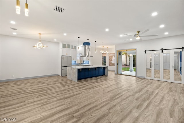 kitchen featuring white cabinets, hanging light fixtures, ceiling fan, a barn door, and stainless steel refrigerator