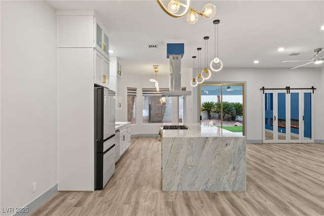 kitchen featuring a center island, hanging light fixtures, a barn door, island range hood, and white cabinetry