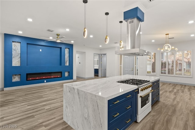 kitchen featuring a center island, ceiling fan with notable chandelier, hanging light fixtures, gas range, and island exhaust hood