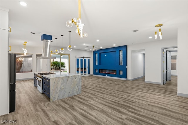 kitchen featuring high end stainless steel range, a barn door, range hood, decorative light fixtures, and light stone counters