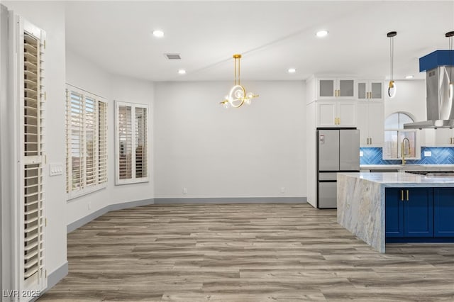 kitchen featuring light stone countertops, hanging light fixtures, stainless steel fridge, decorative backsplash, and white cabinets