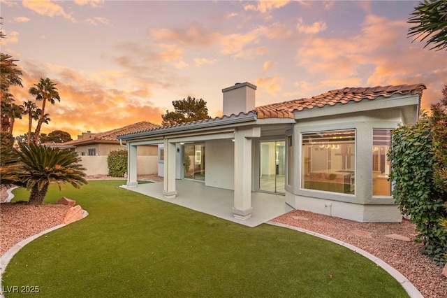 back house at dusk featuring a yard and a patio area