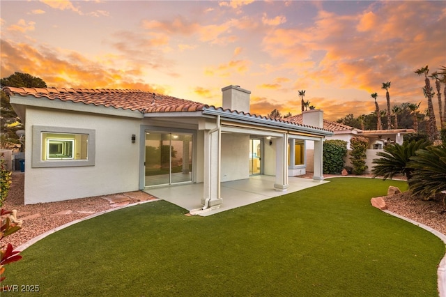 back house at dusk featuring a yard and a patio