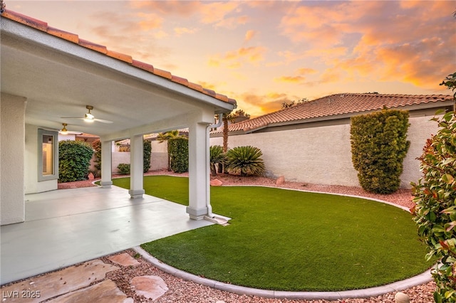 yard at dusk featuring ceiling fan and a patio area