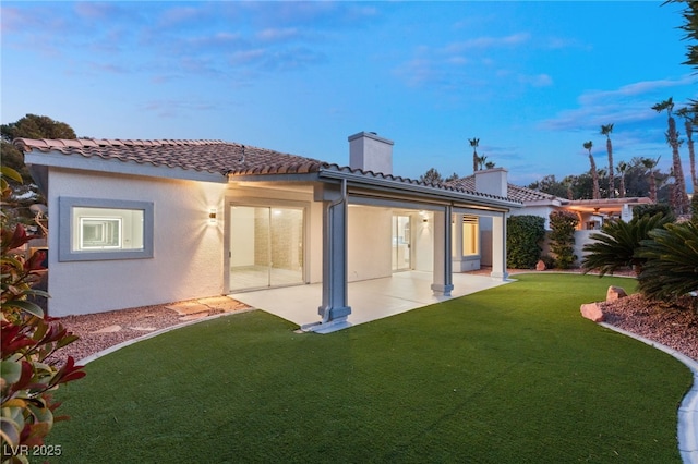 back house at dusk with a patio area and a yard