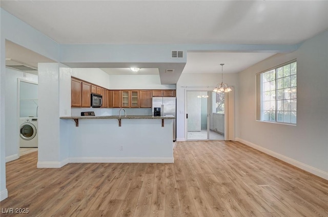 1701 King James St Unit 101, Las Vegas, NV 89144 - kitchen featuring washer / dryer, brown cabinetry, a peninsula, a breakfast bar area, and stainless steel fridge