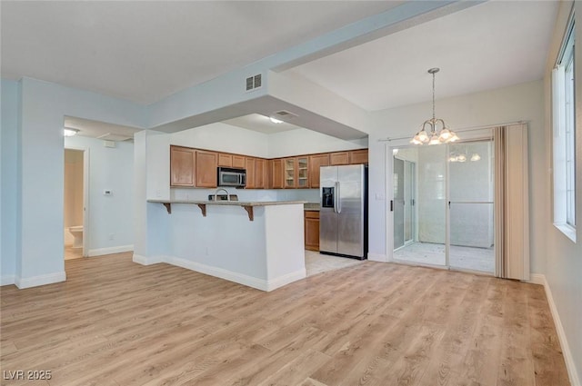 1701 King James St Unit 101, Las Vegas, NV 89144 - kitchen with appliances with stainless steel finishes, brown cabinetry, a peninsula, a kitchen breakfast bar, and glass insert cabinets