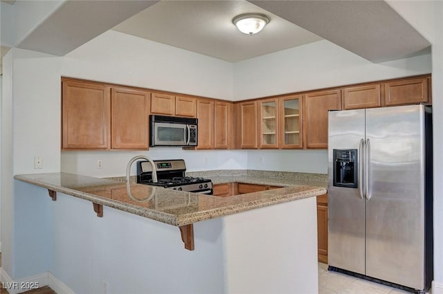 1701 King James St Unit 101, Las Vegas, NV 89144 - kitchen with appliances with stainless steel finishes, brown cabinets, a peninsula, light stone counters, and glass insert cabinets