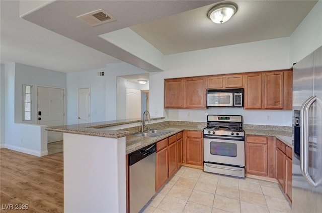 1701 King James St Unit 101, Las Vegas, NV 89144 - kitchen with stainless steel appliances, a sink, a peninsula, light stone counters, and brown cabinets