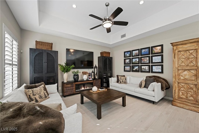 living room with a tray ceiling, ceiling fan, and light hardwood / wood-style floors