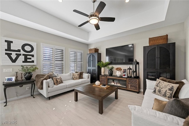 living room featuring light hardwood / wood-style floors, a raised ceiling, and ceiling fan