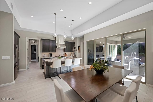 dining room with ceiling fan, a tray ceiling, and light hardwood / wood-style flooring