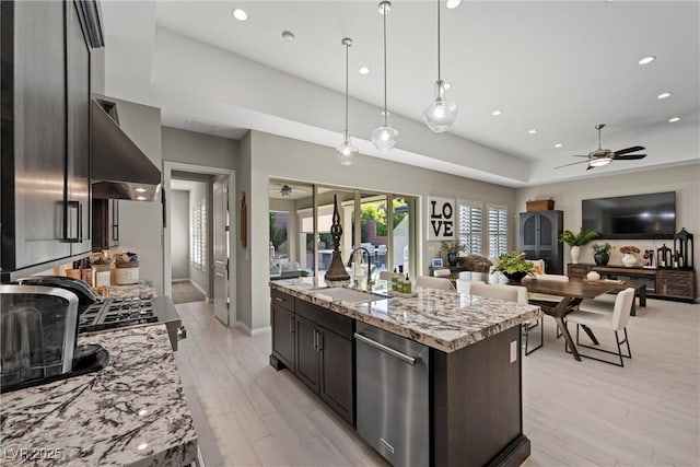 kitchen with light stone counters, stainless steel dishwasher, a kitchen island with sink, sink, and decorative light fixtures