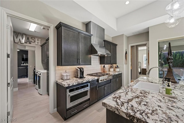 kitchen with sink, wall chimney exhaust hood, tasteful backsplash, independent washer and dryer, and appliances with stainless steel finishes